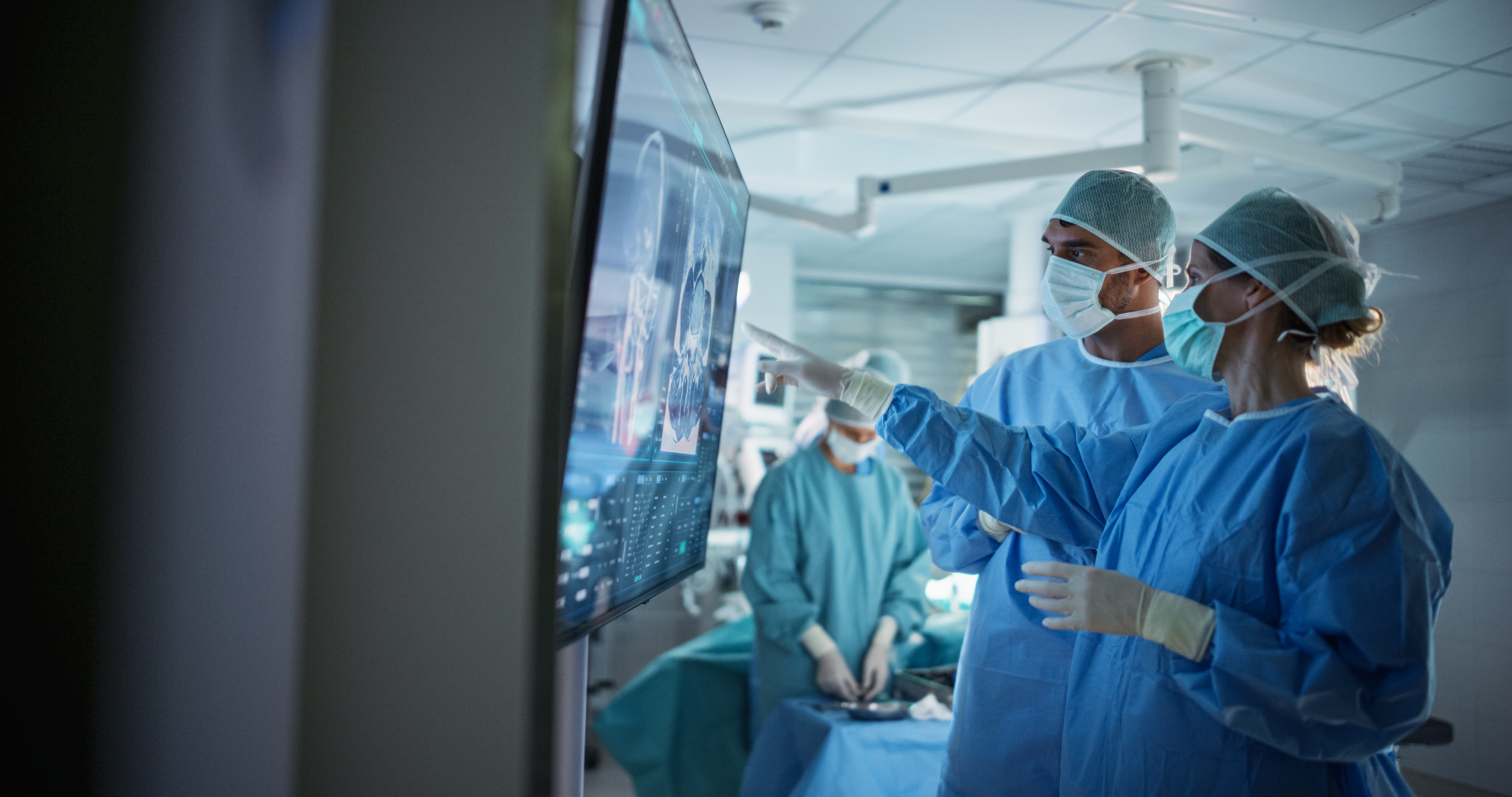 Portrait of a Young Female and Male Surgeons Reviewing Patient's Scans on a Large Screen in a Dimly Lit Operating Room. Their Team of Assistants and Nurses Preparing for a Life-Saving Procedure